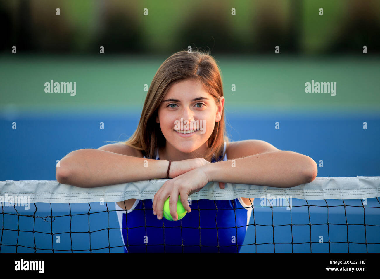 Ritratto di sorridente ragazza adolescente appoggiato su di un campo da tennis net Foto Stock