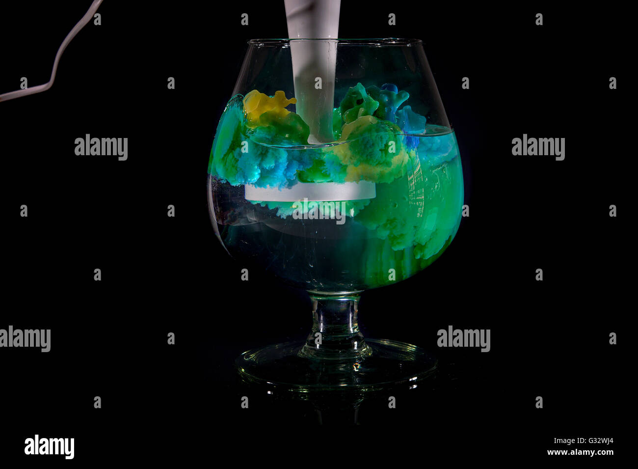 Giallo e blu vernice acrilica mescolata in un bicchiere di acqua Foto Stock