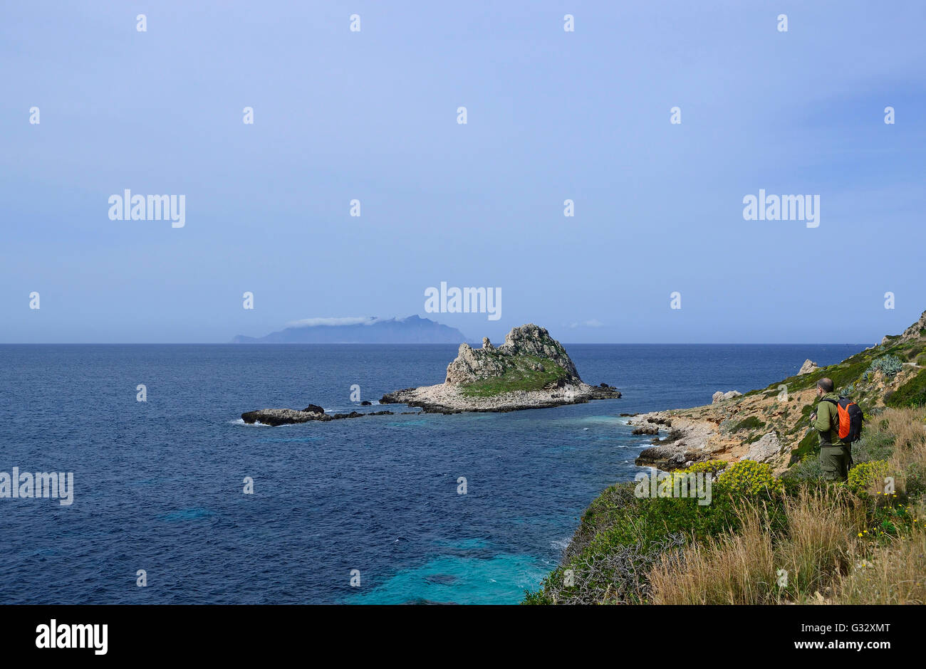 Talia, Sicilia, isole Egadi, isola di Levanzo, escursionista su un sentiero costiero affacciato sul mare con isola Faraglione in background Foto Stock