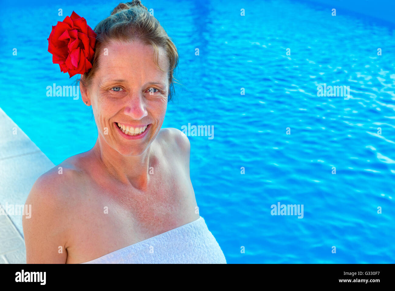 Unione donna di mezza età con una rosa rossa nei capelli e gli asciugamani per il bagno di nuoto Foto Stock