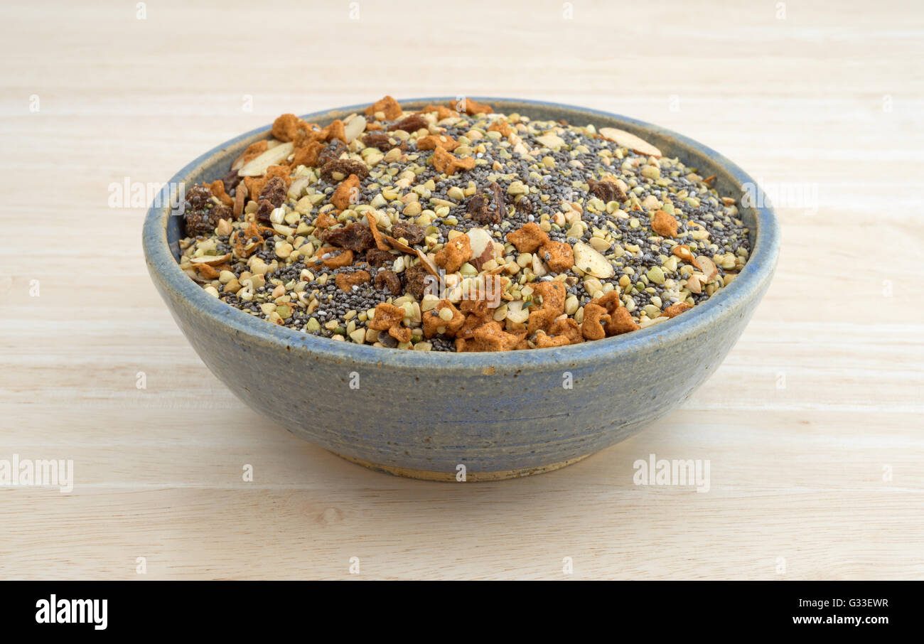 Il gres vecchia ciotola riempita con secca Cereali per la prima colazione consiste di chia semi, frutta a guscio e frutta secca su una tavola di legno alto. Foto Stock