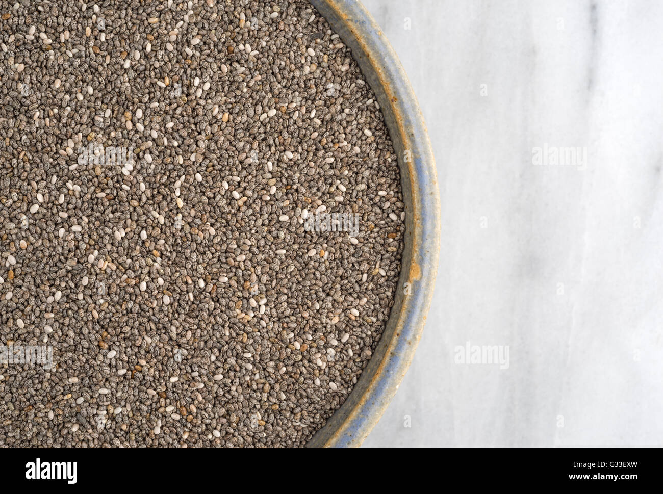 Top vista ravvicinata di un vecchio recipiente di ceramica riempito con organici chia semi sul marmo di un tagliere. Foto Stock