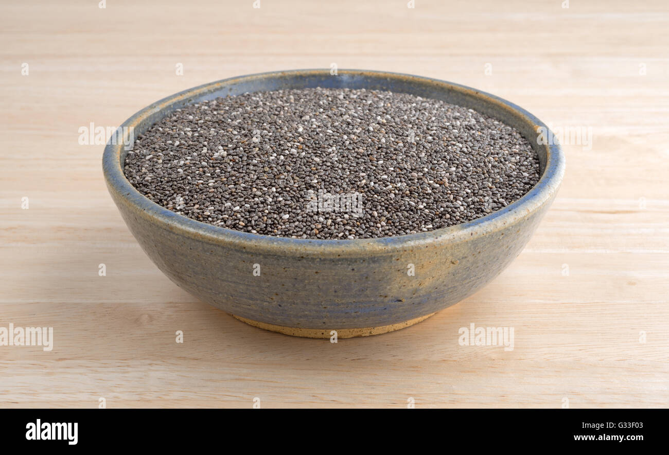 Un vecchio recipiente di ceramica riempito con organici semi di chia su una tavola di legno alto. Foto Stock