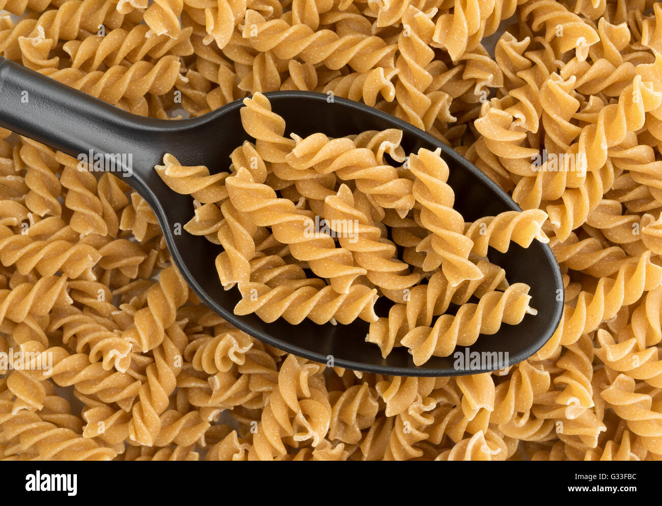 Una porzione di fusilli di grano intero pasta biologica su un cucchiaio di nero sulla sommità di uno strato di pasta. Foto Stock