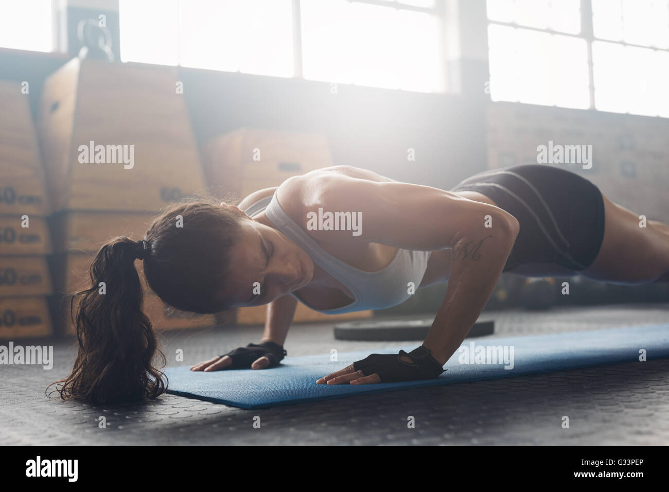 Colpo di giovane donna facendo push-up presso la palestra. Forte atleta femminile fa pushups sul tappeto di esercizio in palestra. Femmina di esercitare su Foto Stock
