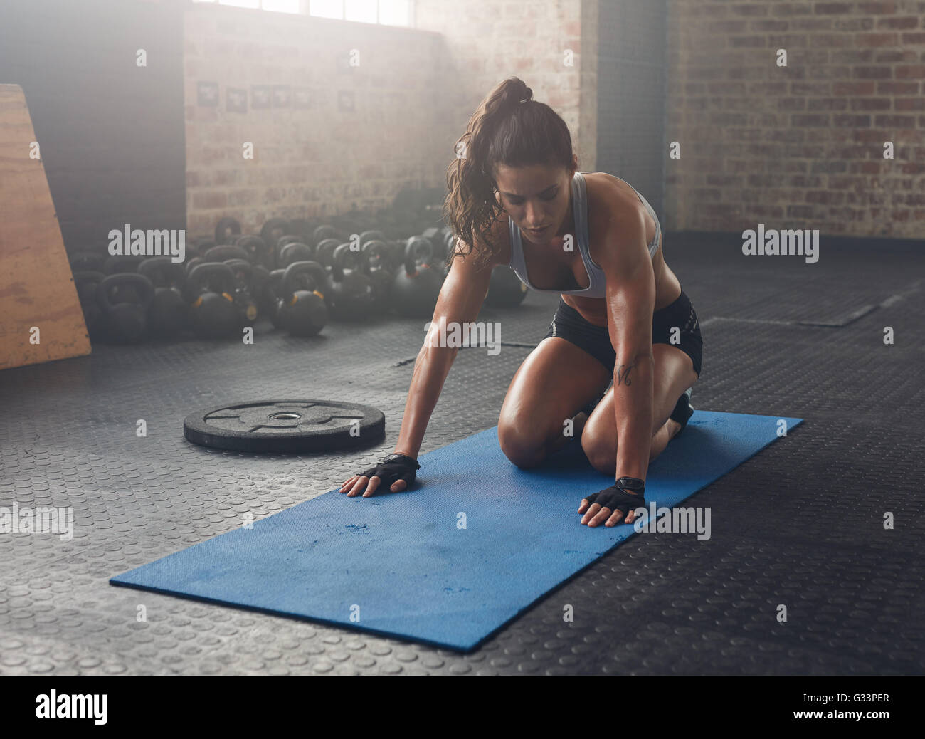 Piscina colpo di donna muscolare per gli esercizi in palestra. Centro fitness donna seduta sul tappetino di esercizio. Foto Stock