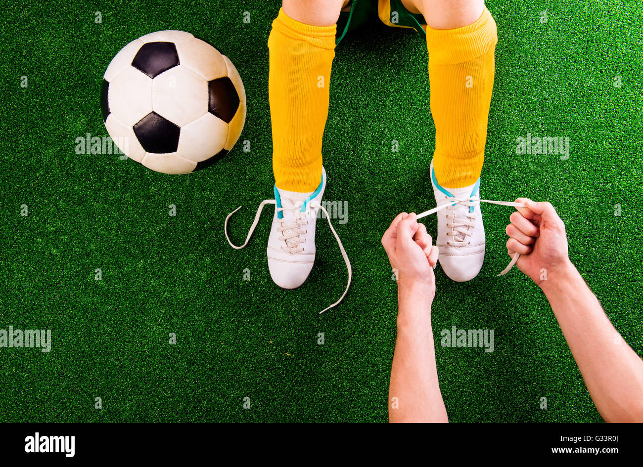 Padre irriconoscibile la legatura lacci delle scarpe a suo figlio, calcio playe Foto Stock