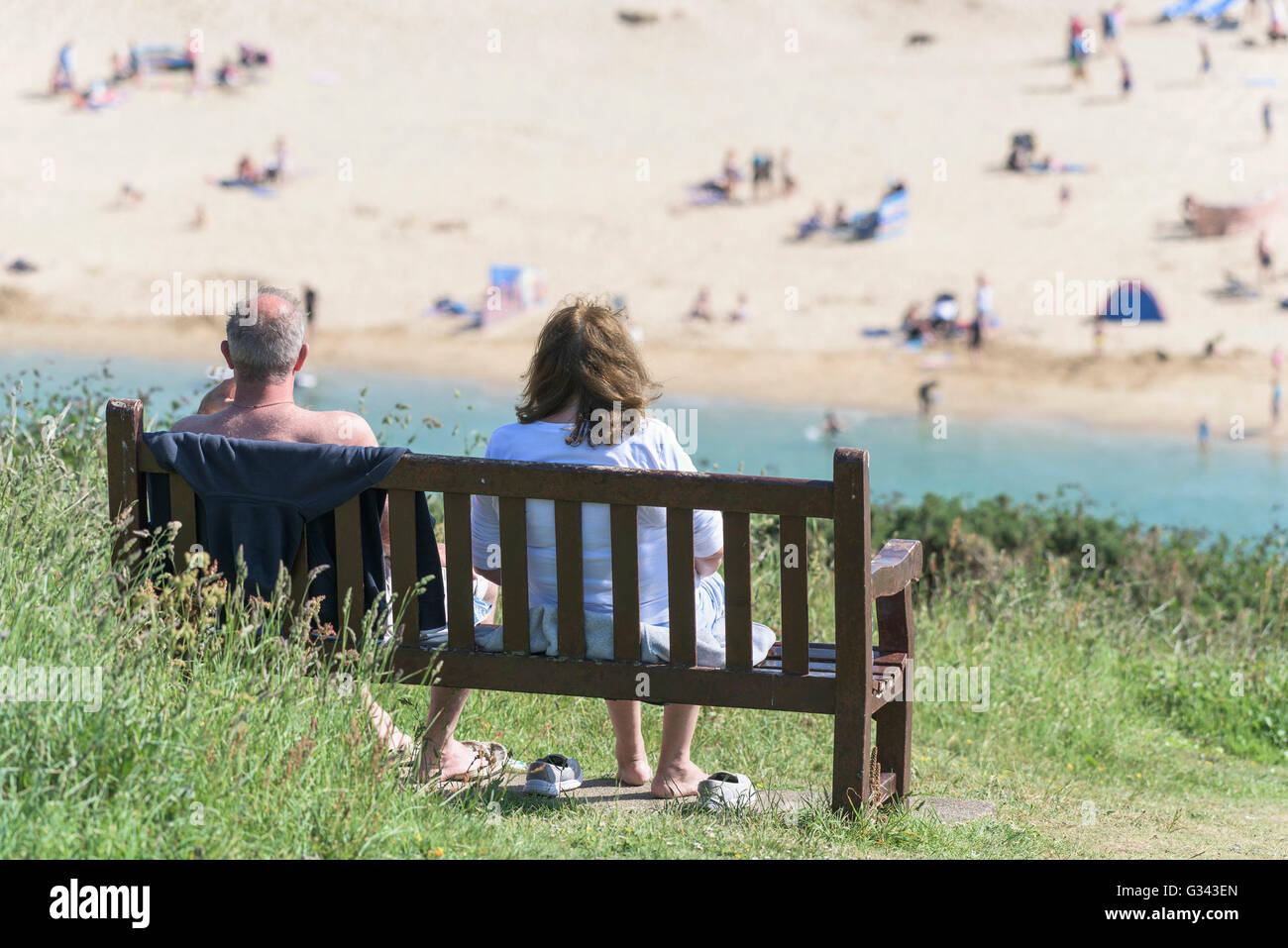 Un paio di vacanzieri godere il sole come loro siedono su una panchina affacciata Crantock Beach in Newquay, Cornwall. Foto Stock