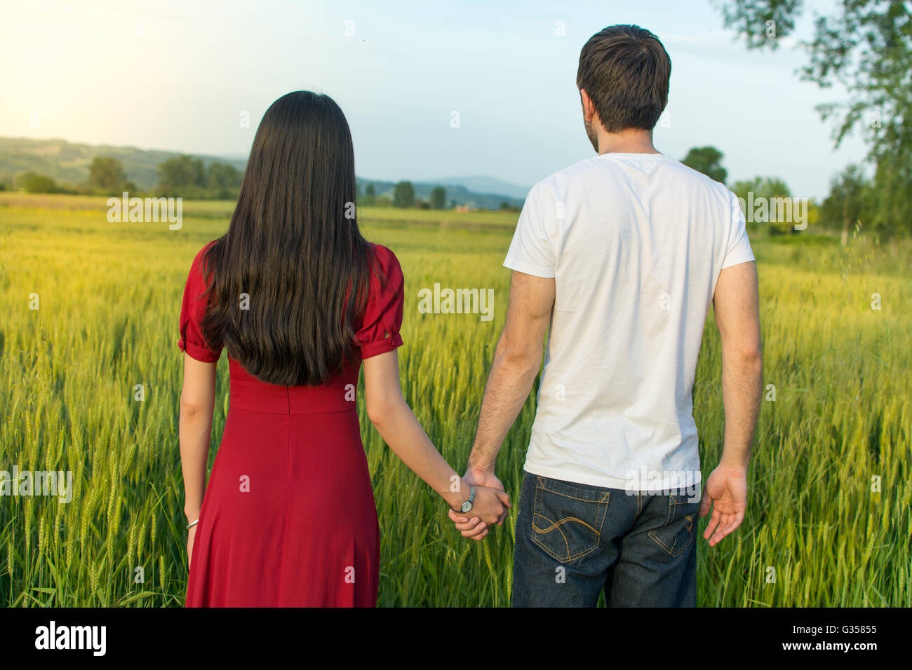 Giovane tenendo le mani in un campo di grano rivolta verso il tramonto Foto Stock