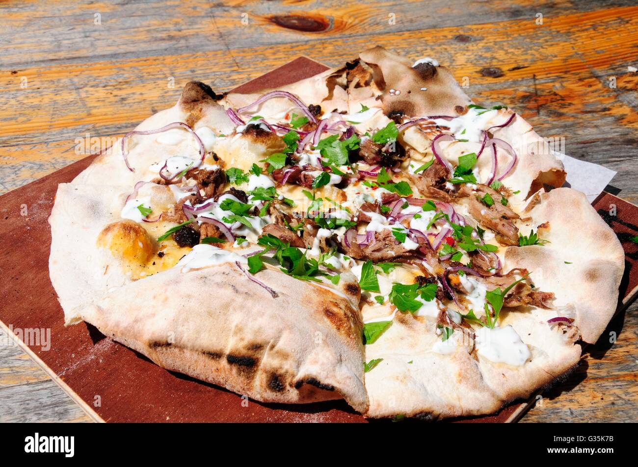 Pizza al forno a legna con agnello yogurt cipolla rossa e coriandolo su una tavola in legno rustico Foto Stock