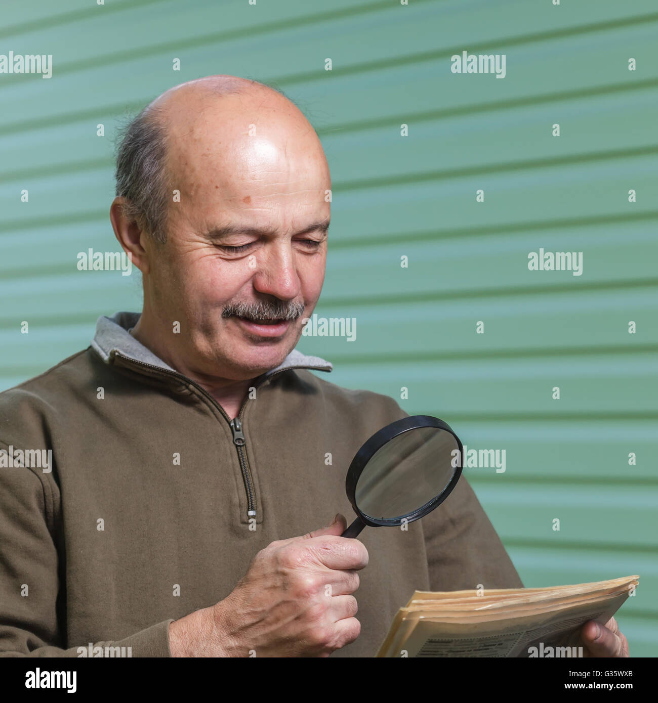 Titolare di pensione o di rendita legge annuncio nel giornale, guardando attraverso una lente di ingrandimento. problemi di visione nella terza età Foto Stock
