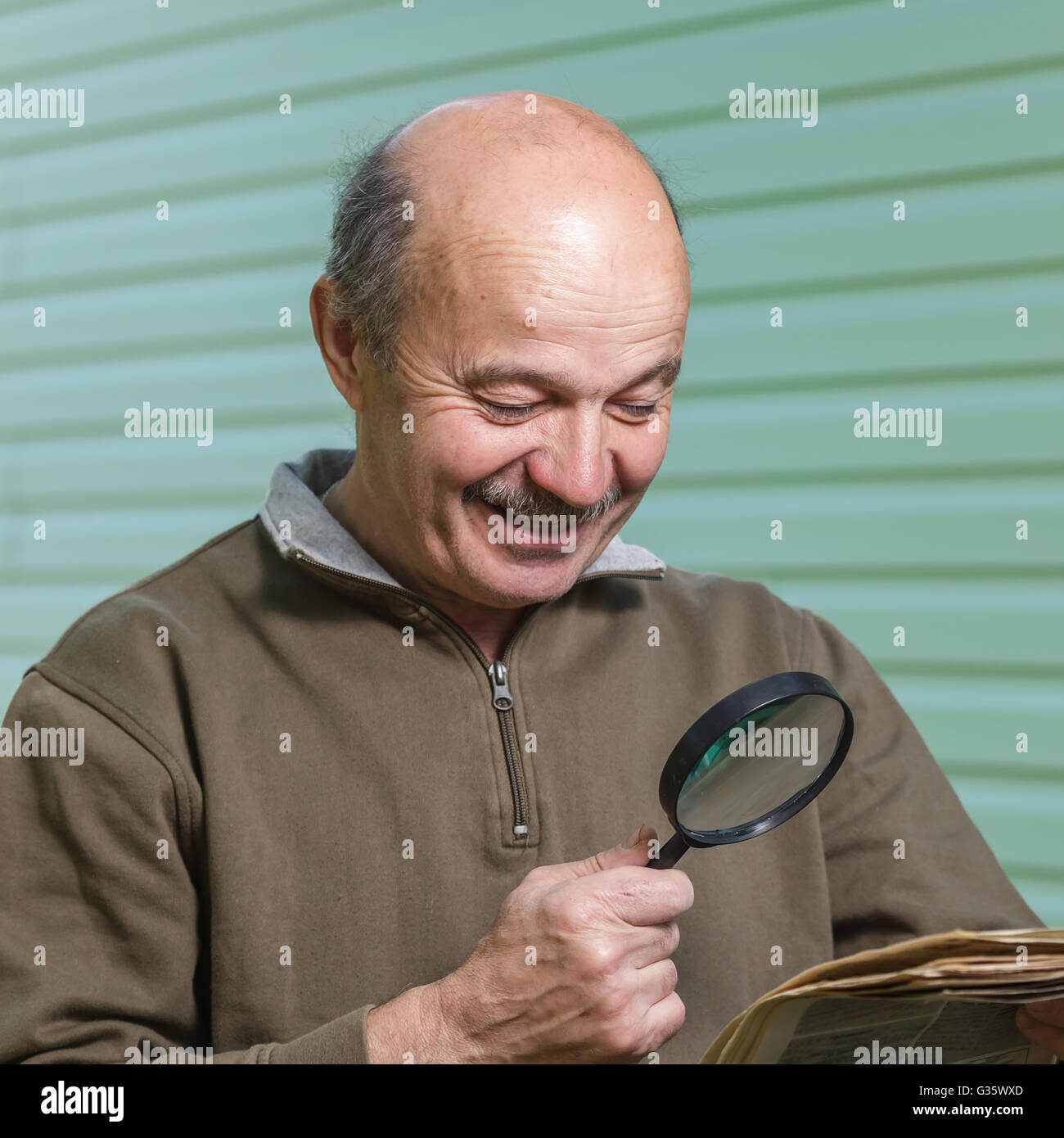 Il pensionato legge la pubblicità sul giornale, guardando attraverso una lente d'ingrandimento. problemi di vista in età avanzata Foto Stock