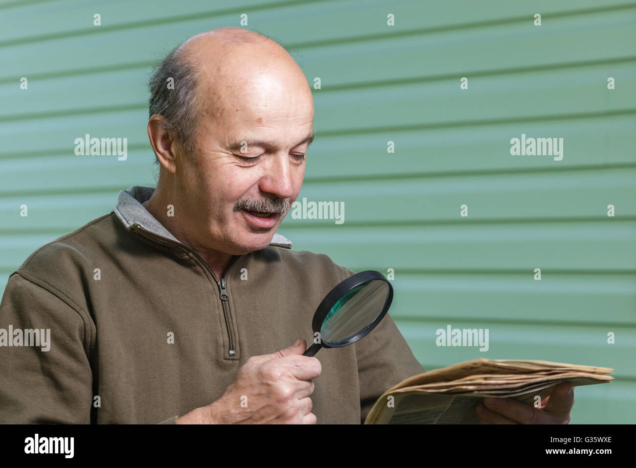 Titolare di pensione o di rendita legge annuncio nel giornale, guardando attraverso una lente di ingrandimento. problemi di visione nella terza età Foto Stock