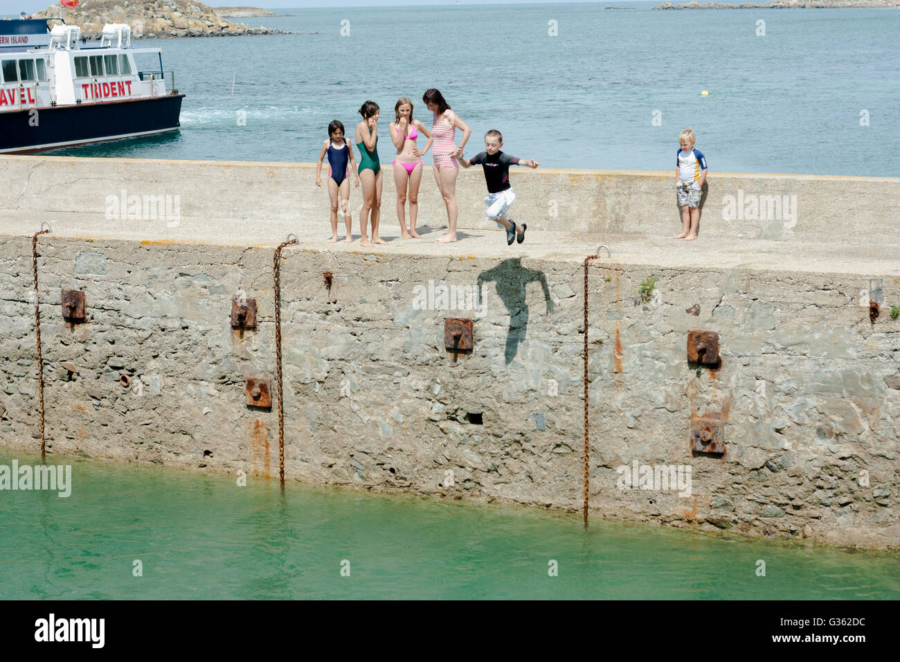 I ragazzi e le ragazze del salto dal pontile a mare al porto di Herm Island, isola di canale Foto Stock