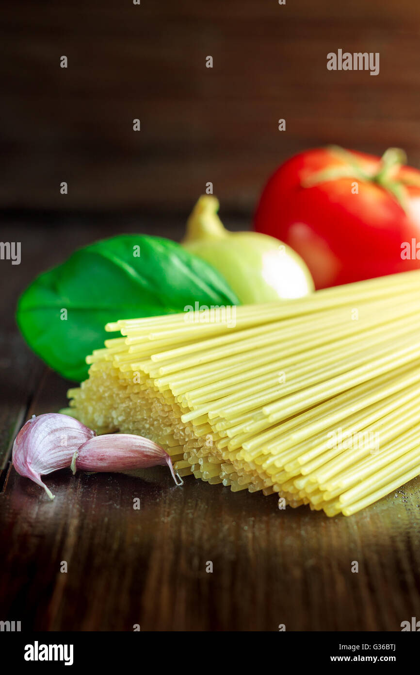 Spaghetti crudo su legno scuro dello sfondo con pomodoro, basilico, l'aglio e la cipolla. Preparazione per la cottura di spaghetti. Spazio di copia Foto Stock