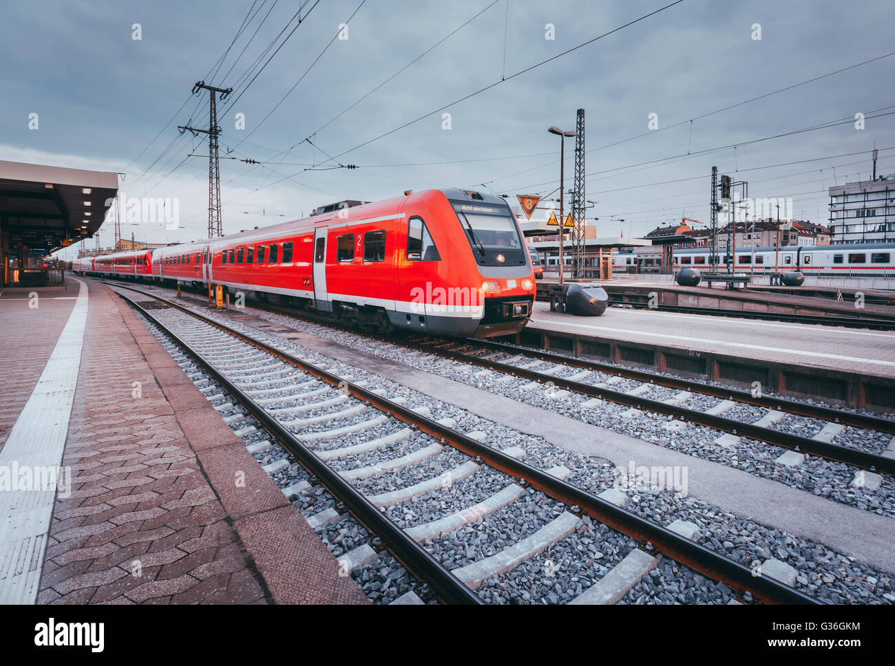 Stazione ferroviaria con rosso moderno treno passeggeri al tramonto a Norimberga, Germania. Ferrovia con tonificazione vintage. Landsc industriale Foto Stock