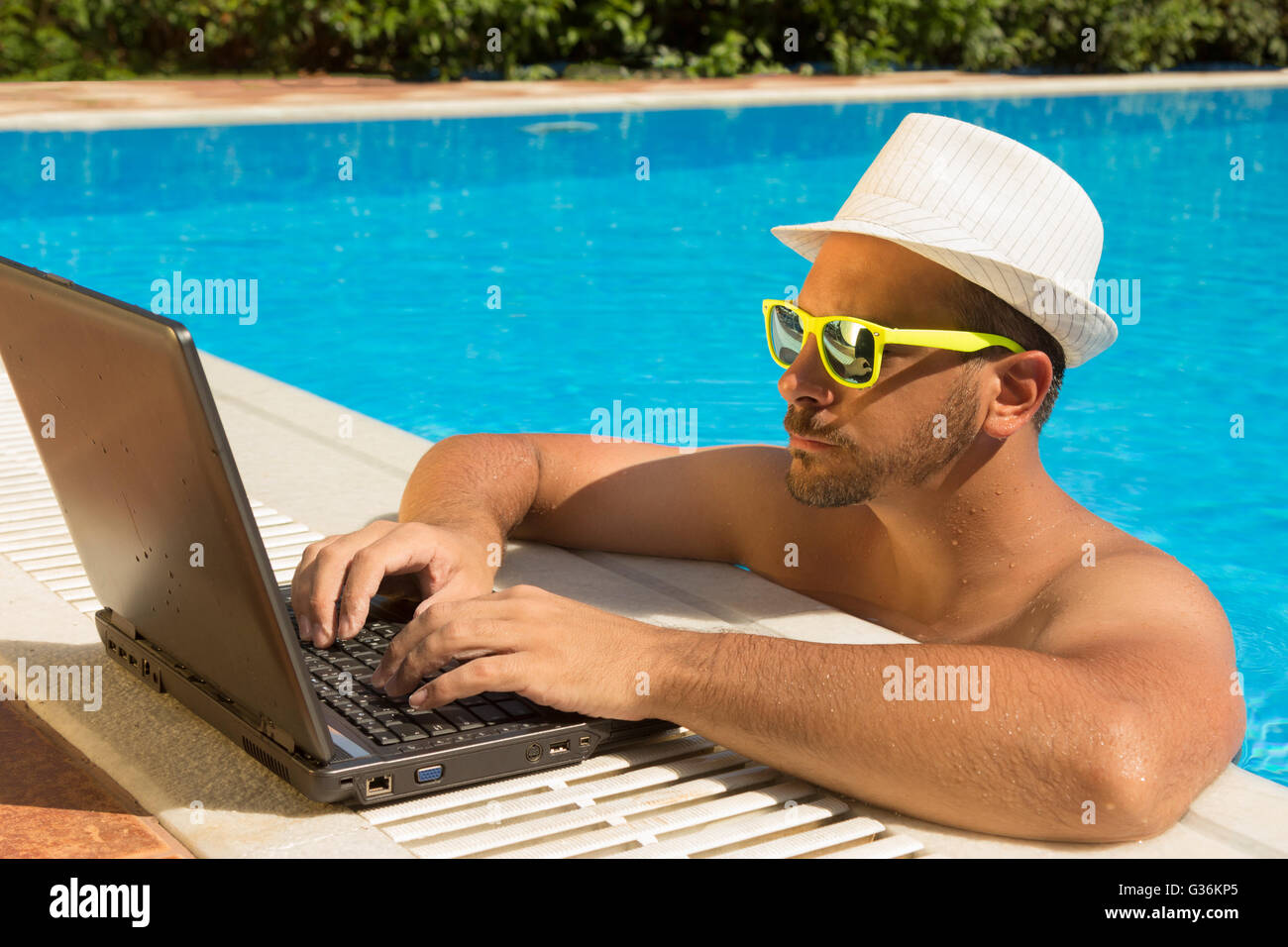 Uomo al lavoro su laptop a bordo piscina Foto Stock