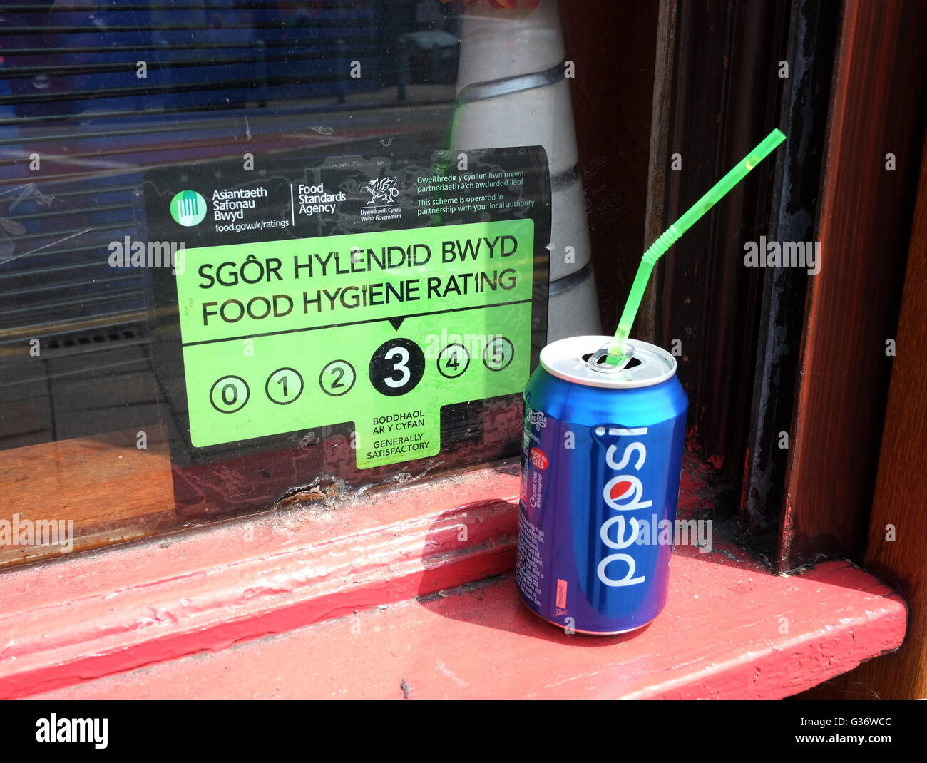 Bi linguale igiene alimentare segno di rating di 3 in un negozio di Cardiff finestra con una lattina di Pepsi a sinistra sulla finestra del cill. Giugno 2016 Foto Stock