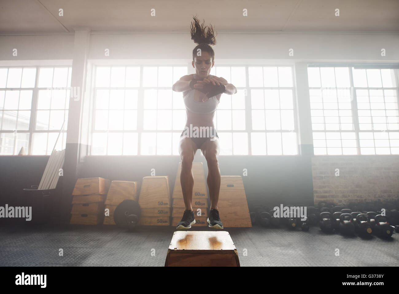 Colpo di giovane donna che lavora fuori con una scatola in palestra. Giovane atleta femminile box jumping in una palestra crossfit. Foto Stock
