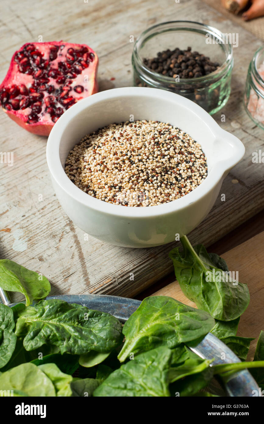 La quinoa in bianco ciotola da una fetta di melograno, grani di pepe, e spinaci Foto Stock