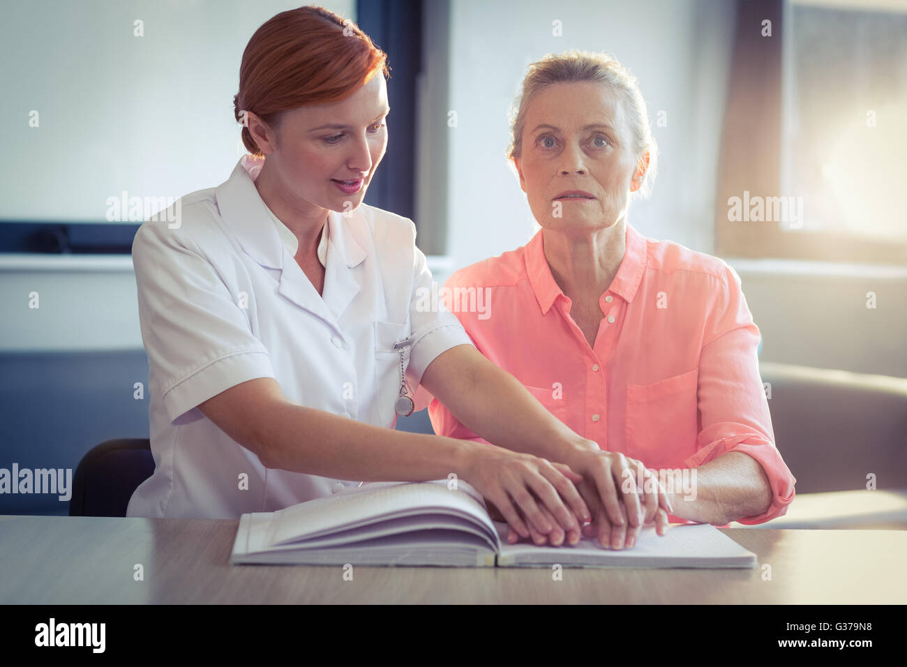 Femmina aiutando infermiere paziente nella lettura del libro in braille Foto Stock