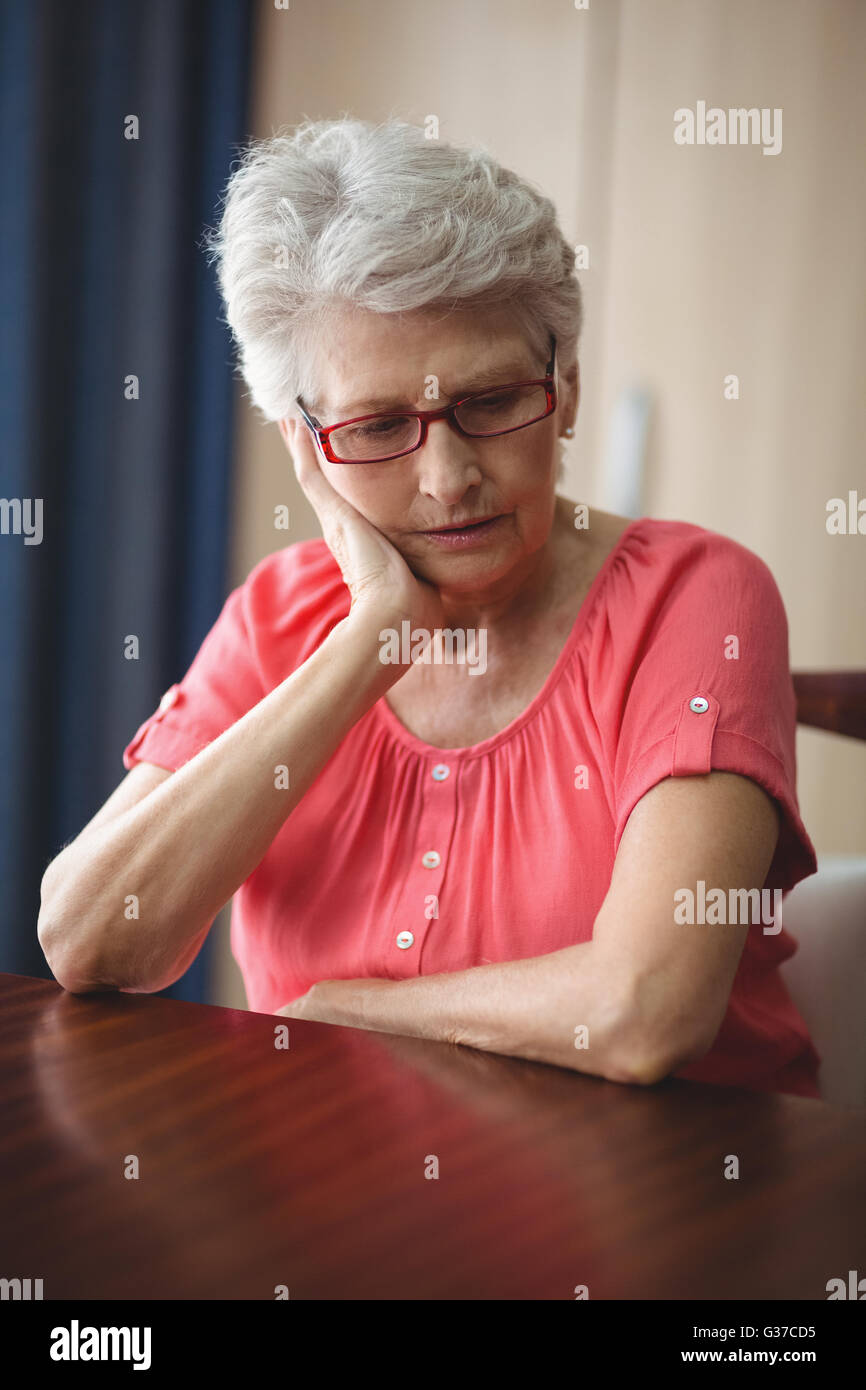 Triste senior donna seduta al tavolo Foto Stock