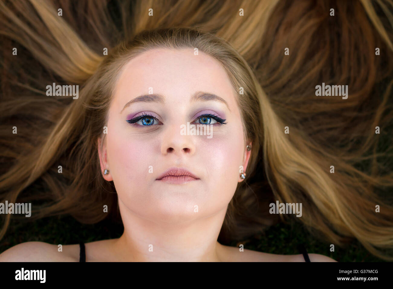 Una bella ragazza adolescente giace sulla terra con la sua lunga, capelli biondi sparsi intorno a lei. Guarda blankly fino alla telecamera Foto Stock