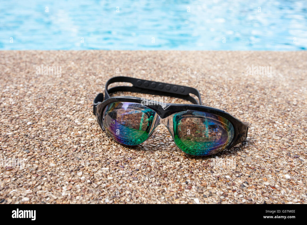 Occhiali per nuoto su un pavimento di cemento con piccola pietra vicino alla piscina. Foto Stock
