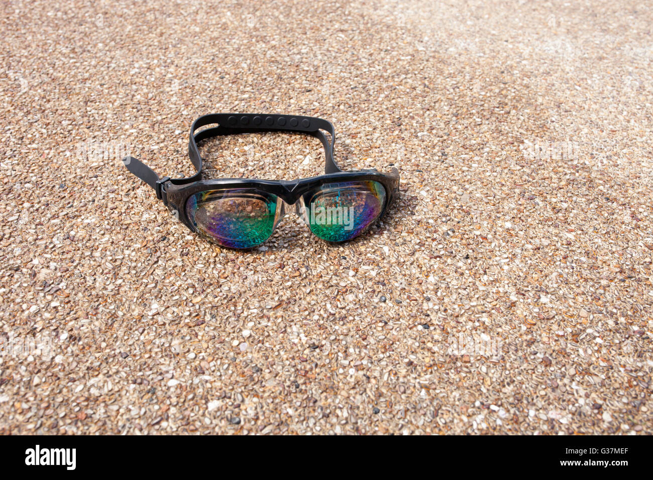 Occhiali per nuoto su un pavimento di cemento con piccola pietra vicino alla piscina. Foto Stock