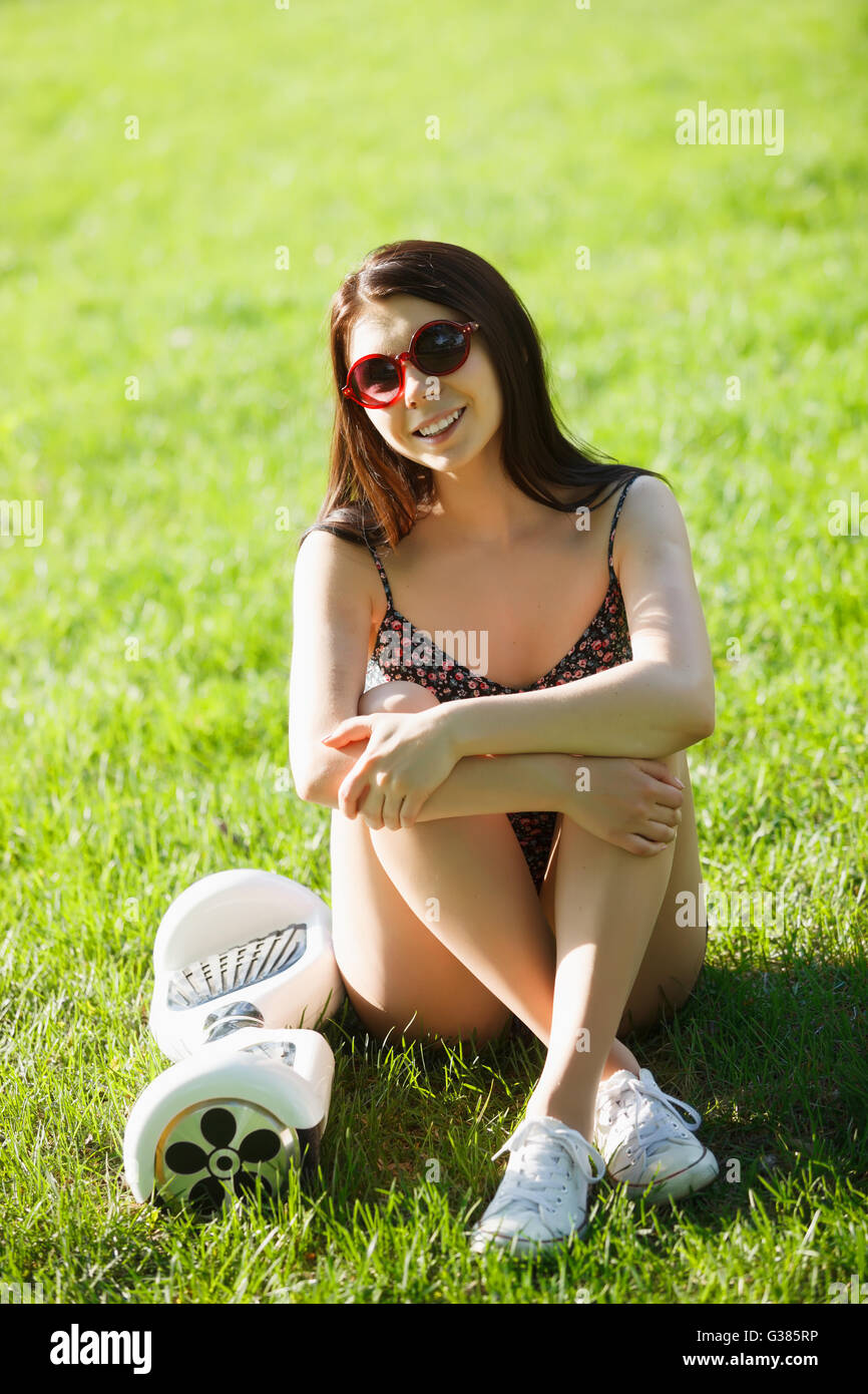 Bruna giovane donna con impianto elettrico mini scheda hover scooter nel parco verde. Buona estate meteo, alla moda tecnologia dei trasporti e modello di cute. Foto Stock