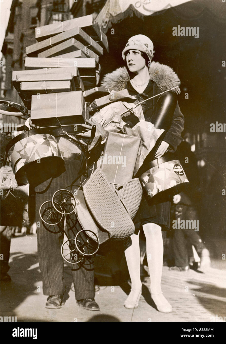 Una donna è stata molto occupata shopping, tanto che la sua helper è nascosta al di sotto di una pila di colli. Data: 1920s Foto Stock