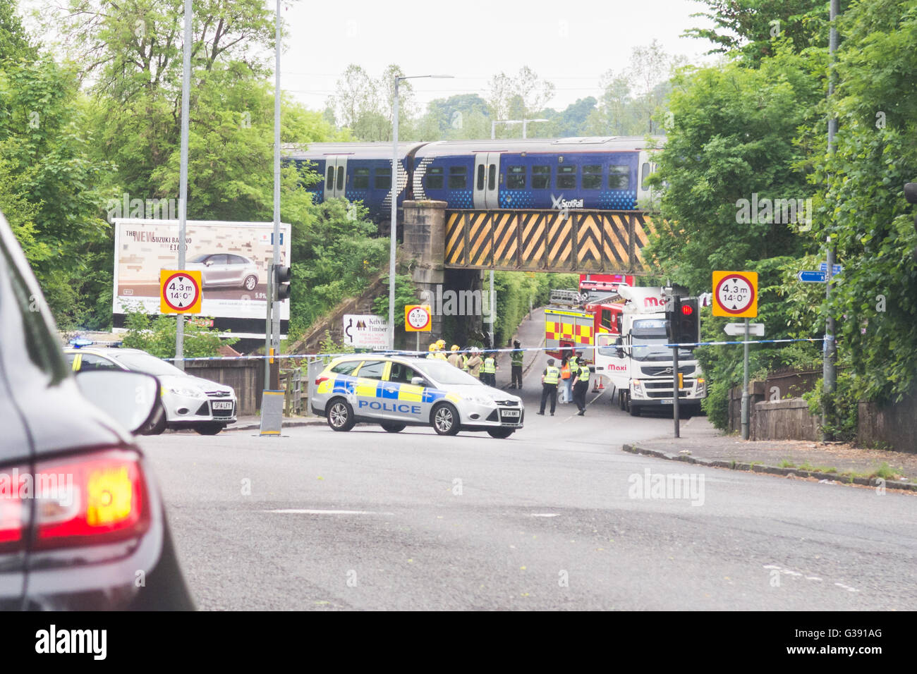 Milngavie, Glasgow, Scotland, Regno Unito. Decimo Giugno, 2016. Treno ScotRail passando al di sopra di un ponte ferroviario in cui un camion è rimasto intrappolato. L'incidente è stato frequentato da forze di polizia e la Scottish servizi antincendio e di soccorso e la strada - in corrispondenza della giunzione di Glasgow Road e Auchenhowie Road - è stato chiuso per qualche tempo durante la mattinata come il camion è stato rimosso. Non vi sono state segnalazioni di lesioni e la strada è stata riaperta. Credito: Kay Roxby/Alamy Live News Foto Stock