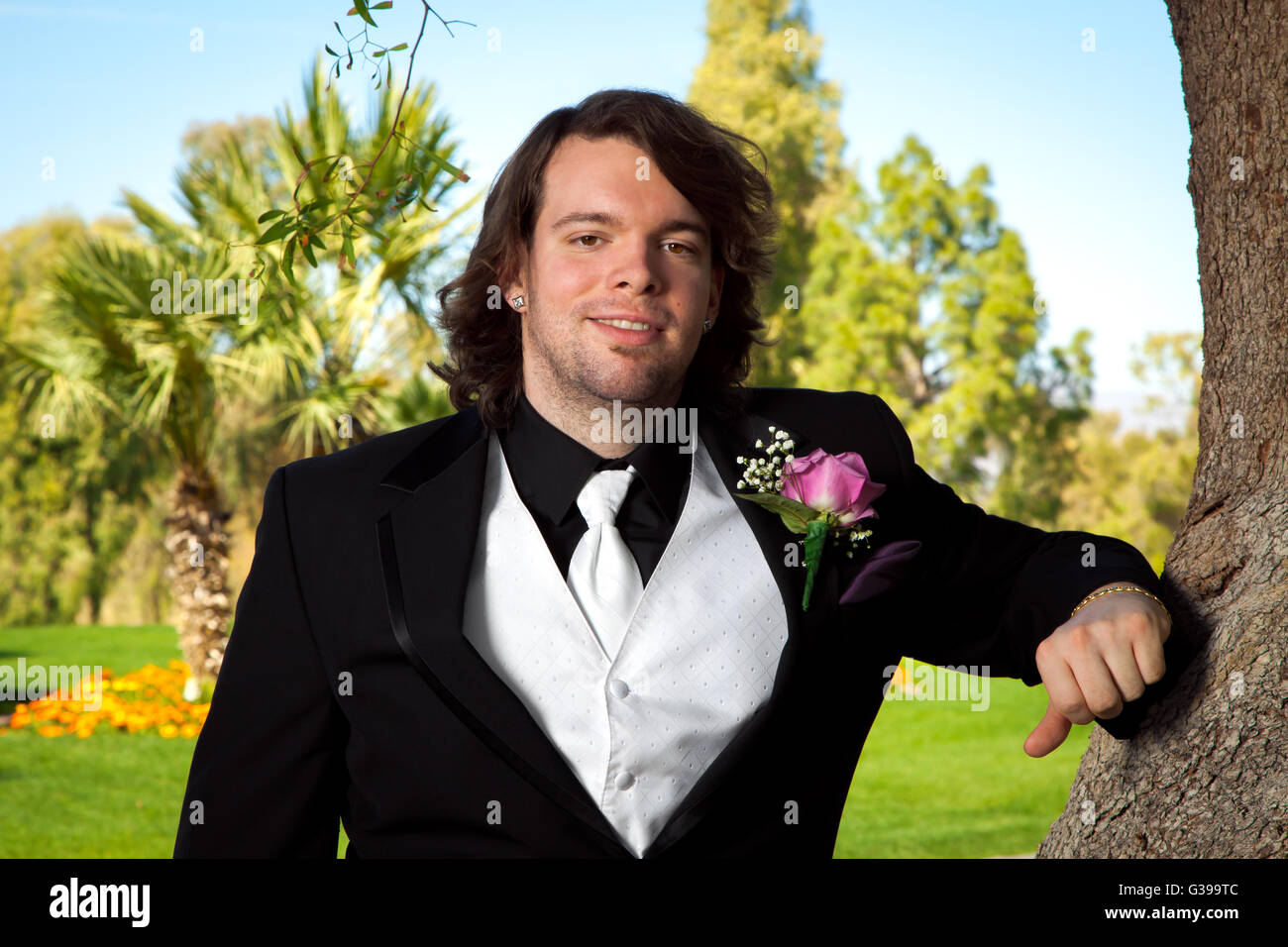 Un groom poggia su una struttura ad albero per il suo giorno di nozze. Egli ha una rosa di rose e boutonniere un bianco Gilet e cravatta. Foto Stock