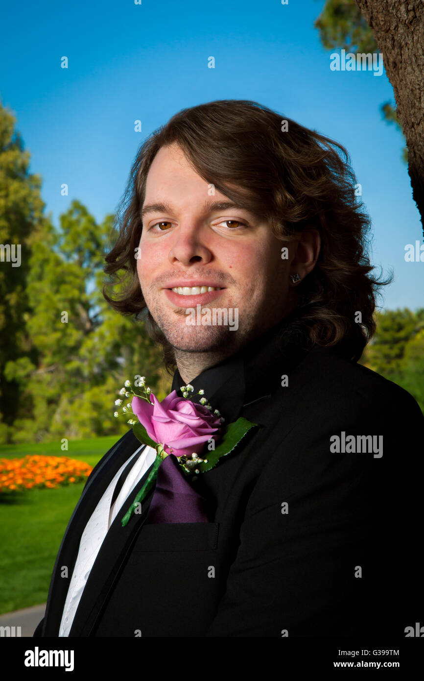 Outdoor ritratto di uno sposo per il suo giorno di nozze. Egli si erge, sorridente alla fotocamera con una rosa boutonnière, stoppia, orecchini, un Foto Stock