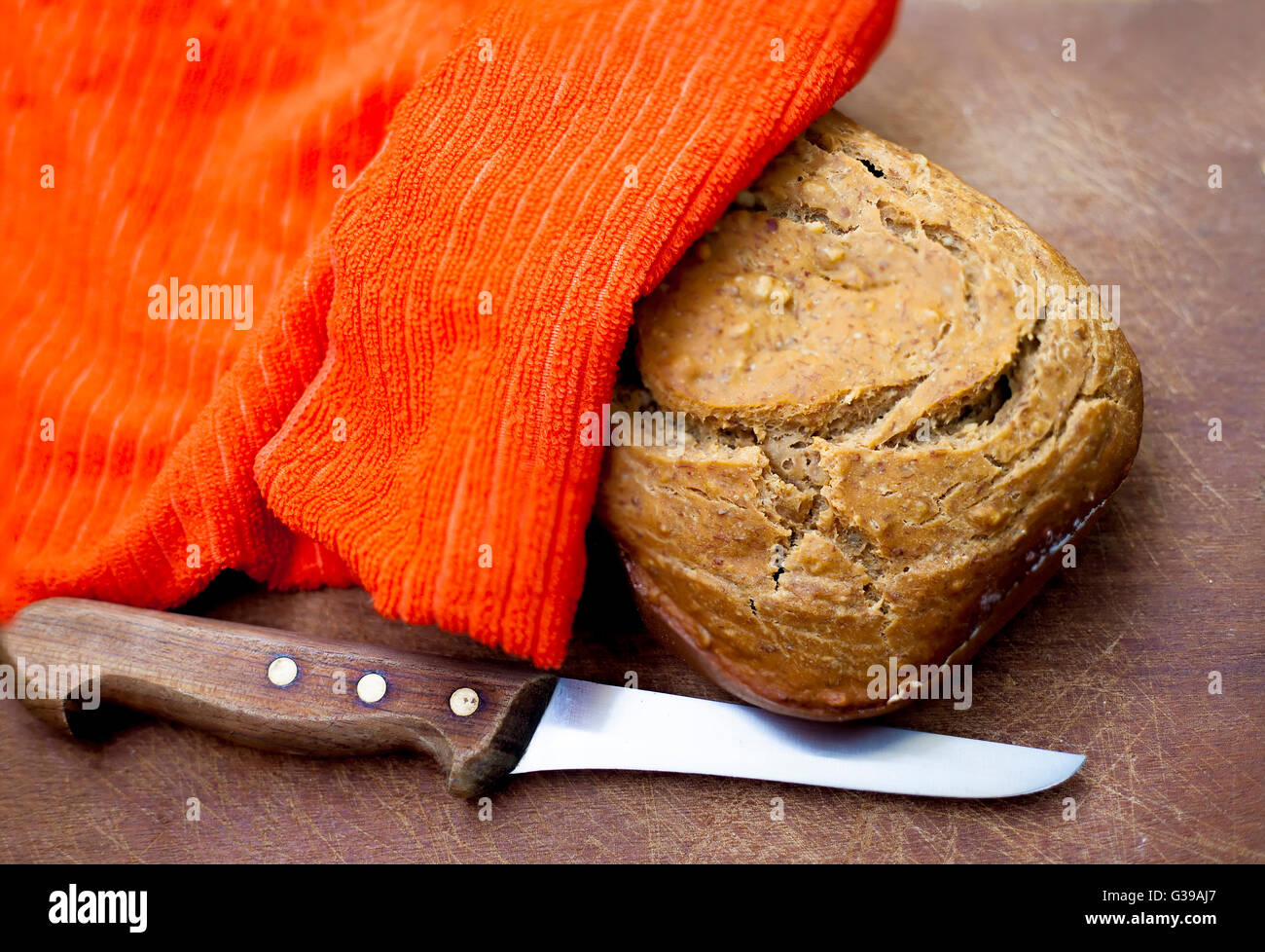 Pane fresco sotto un tovagliolo e con manico in legno coltello su una scheda Foto Stock