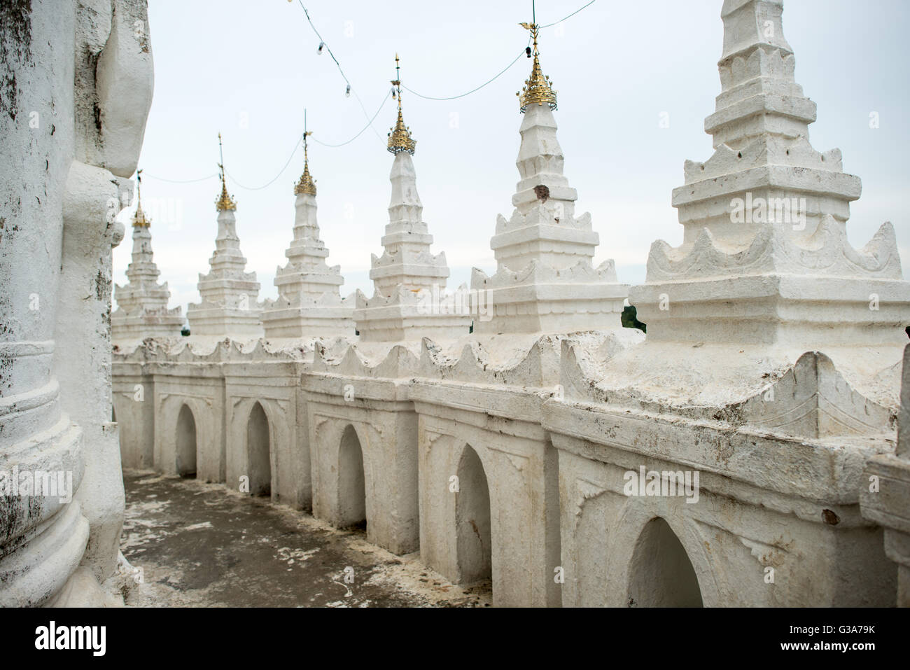 Pagoda di Hsinbyume Dettagli architettonici Mingun Myanmar // MINGUN, Myanmar — i dettagli architettonici della Pagoda di Hsinbyume mostrano la caratteristica architettura del tempio buddista dipinto di bianco. La pagoda, nota anche come Pagoda Myatheindan, fu costruita nel 1816 dal principe Bagyidaw come rappresentazione del sacro Monte Meru dalla cosmologia buddista. La struttura presenta sette terrazze ondulate che simboleggiano le sette catene montuose che circondano il Monte Meru secondo la tradizione buddista. Situata a Mingun lungo il fiume Irrawaddy, la pagoda si trova a circa 11 chilometri a nord di Mandalay. Il tempio co Foto Stock