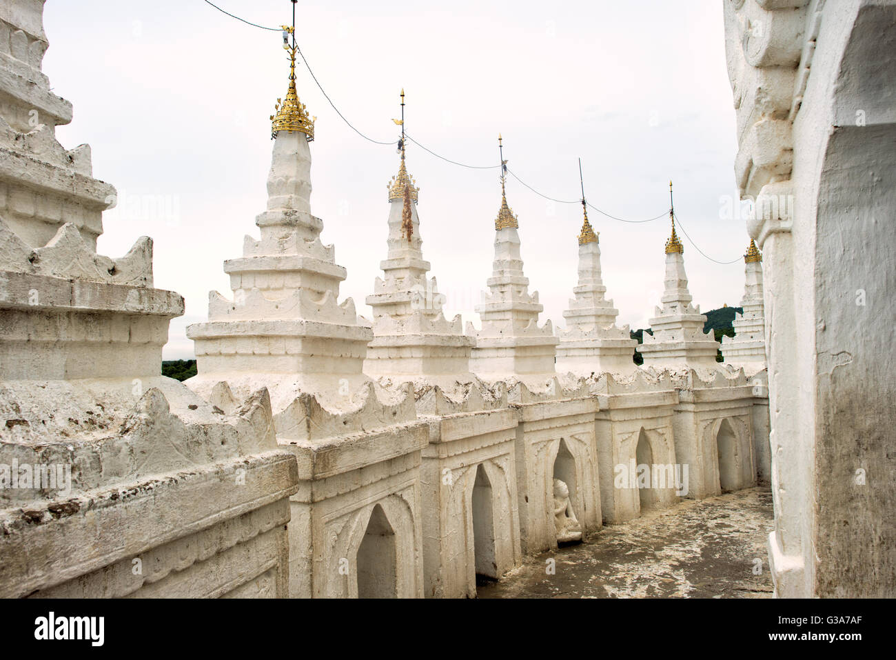 Pagoda di Hsinbyume Dettagli architettonici Mingun Myanmar // MINGUN, Myanmar — i dettagli architettonici della Pagoda di Hsinbyume mostrano la caratteristica architettura del tempio buddista dipinto di bianco. La pagoda, nota anche come Pagoda Myatheindan, fu costruita nel 1816 dal principe Bagyidaw come rappresentazione del sacro Monte Meru dalla cosmologia buddista. La struttura presenta sette terrazze ondulate che simboleggiano le sette catene montuose che circondano il Monte Meru secondo la tradizione buddista. Situata a Mingun lungo il fiume Irrawaddy, la pagoda si trova a circa 11 chilometri a nord di Mandalay. Il tempio co Foto Stock