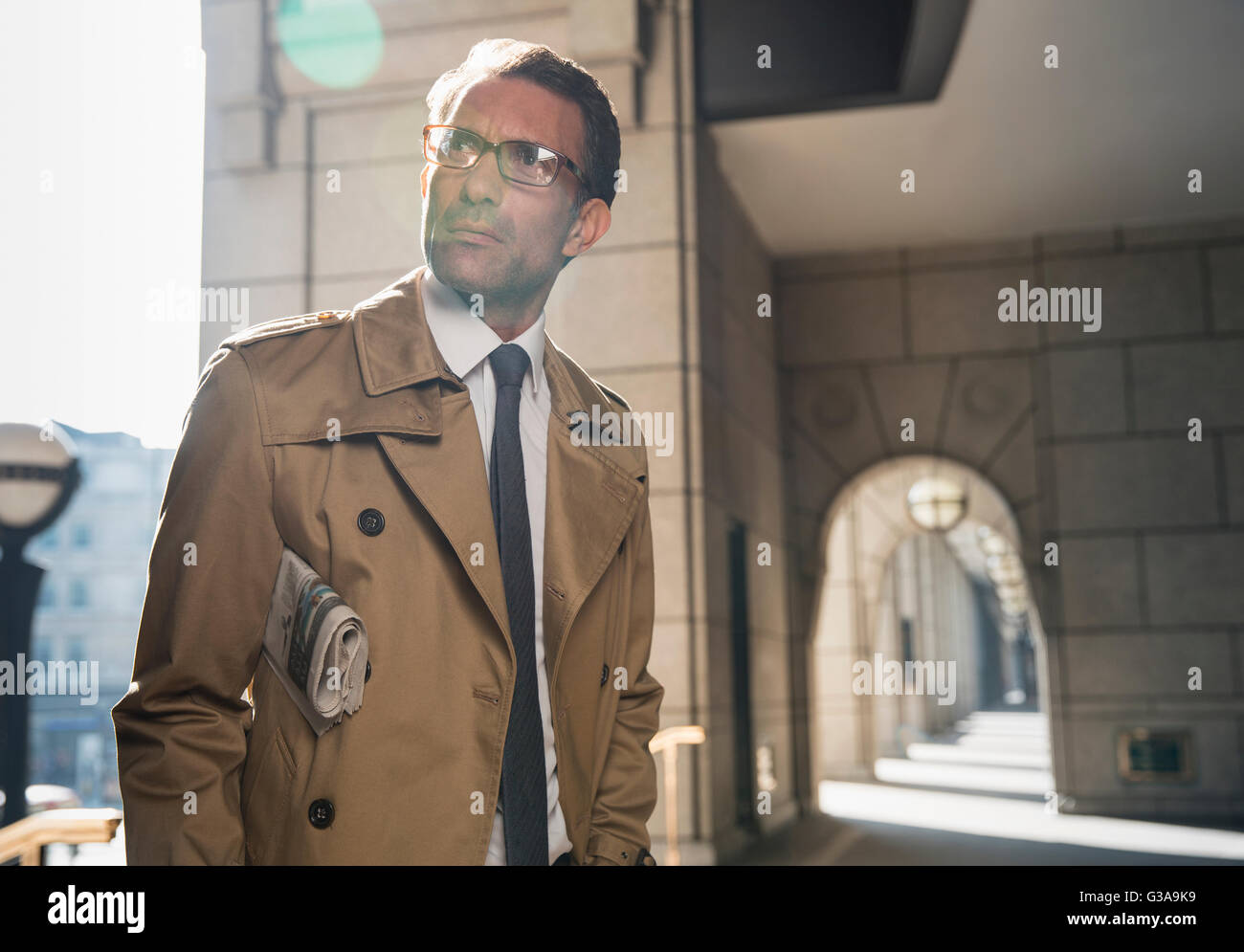 Imprenditore aziendale in trench coat in piedi nel chiostro soleggiato Foto Stock