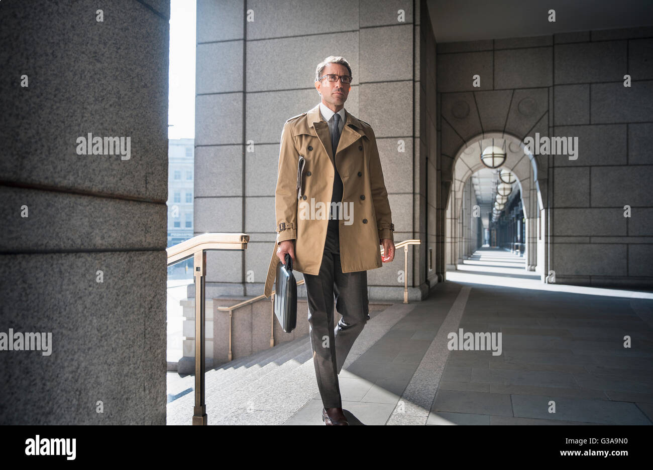 Imprenditore aziendale in trench coat camminando nel chiostro Foto Stock