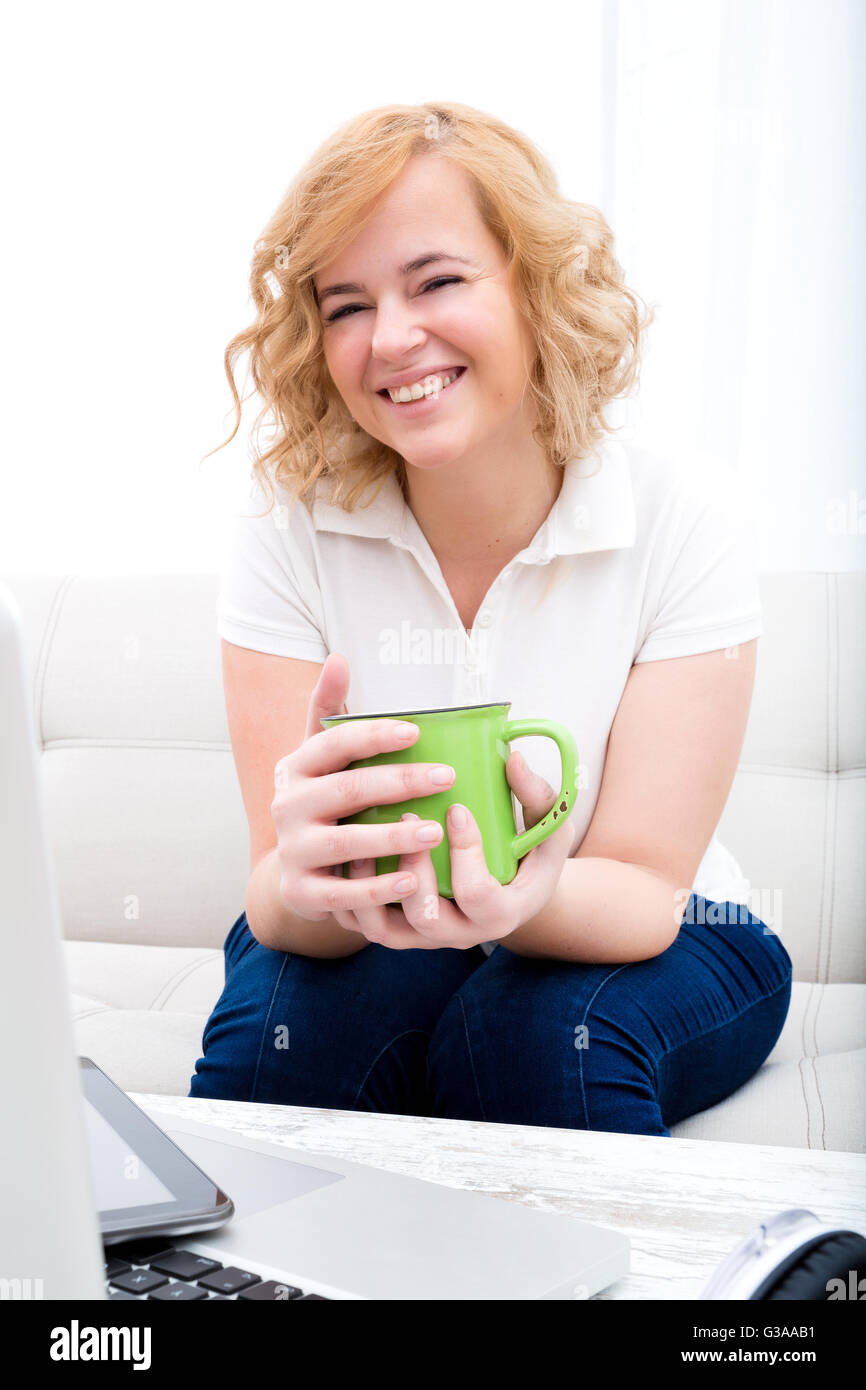 Un giovane Taglie donna seduta su un divano con un Tablet PC e un computer portatile sul tavolo. Foto Stock