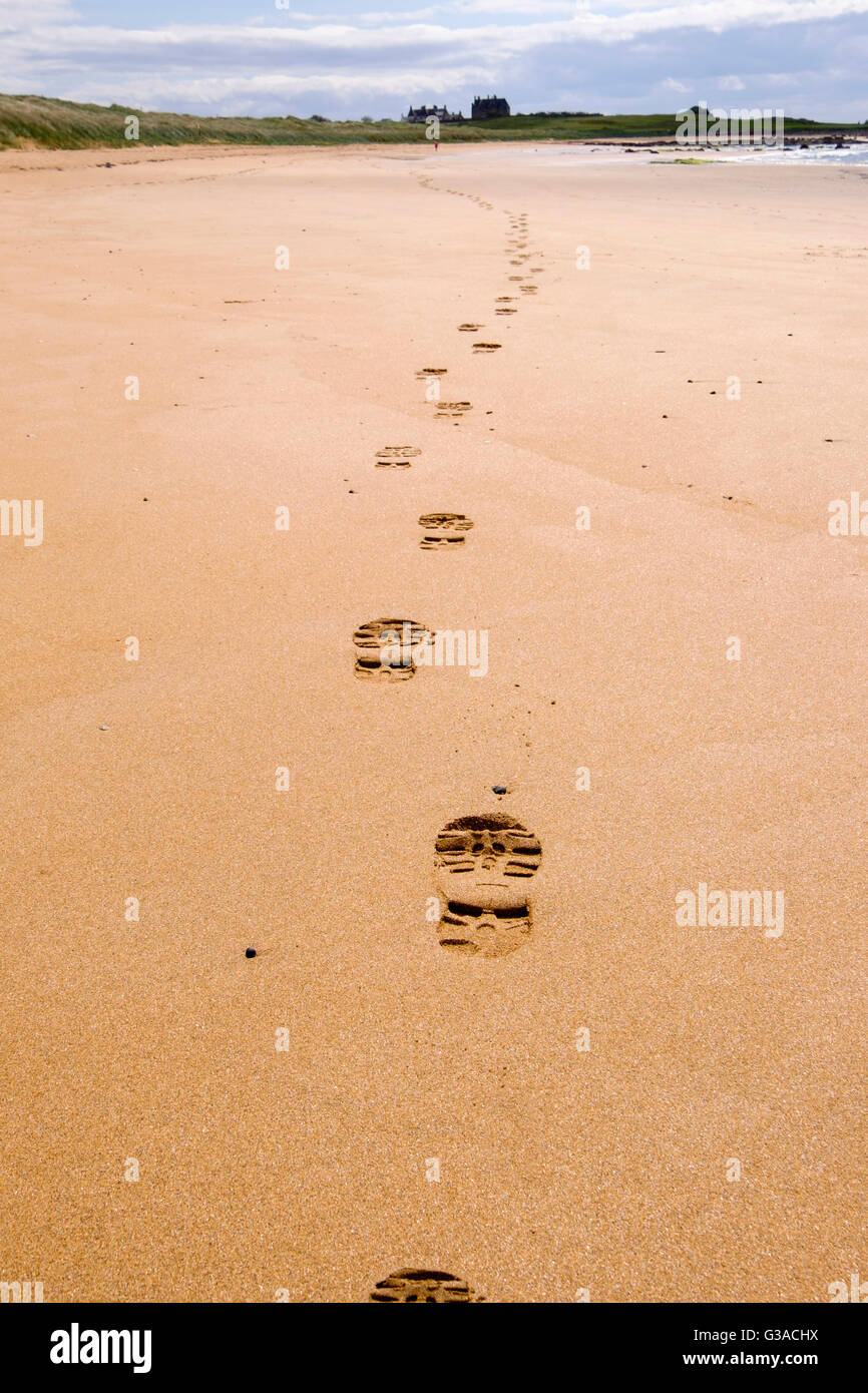 Linea di impronte stampe di boot che portano lontano nella sabbia lungo la Fife Sentiero costiero di bassa marea rotta con walker in distanza. West Beach Elie Scozia UK Foto Stock