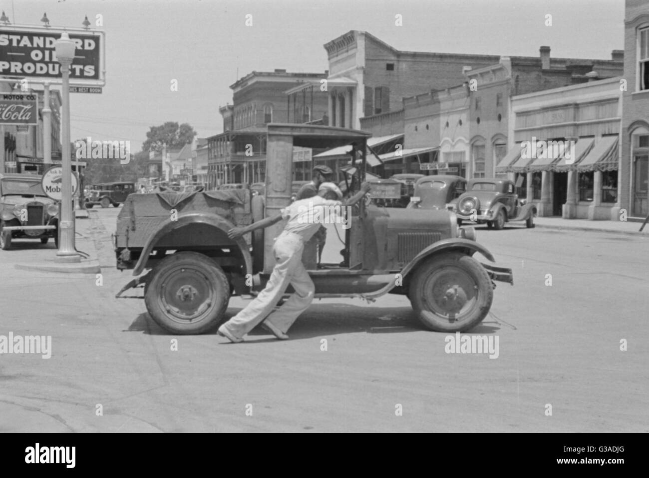 L'uomo spingendo ripartiti auto 1930s. Scena di strada, Greensboro, Alabama, Stati Uniti d'America Data: 1936 Foto Stock