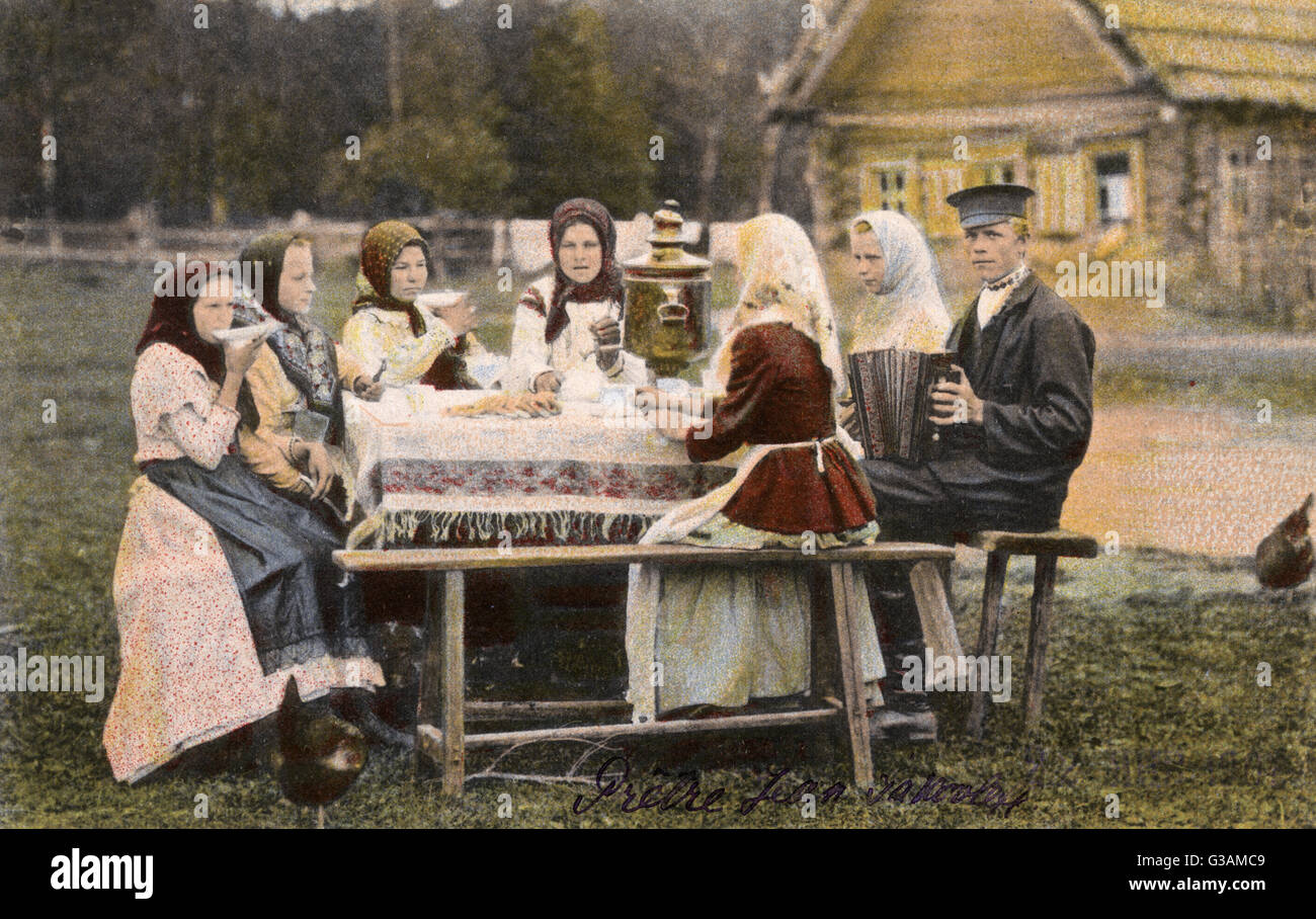 Gli abitanti di un villaggio russo bere il tè (versata da un samovar) come essi ascoltare una giovane gent di suonare la fisarmonica. Data: circa 1906 Foto Stock