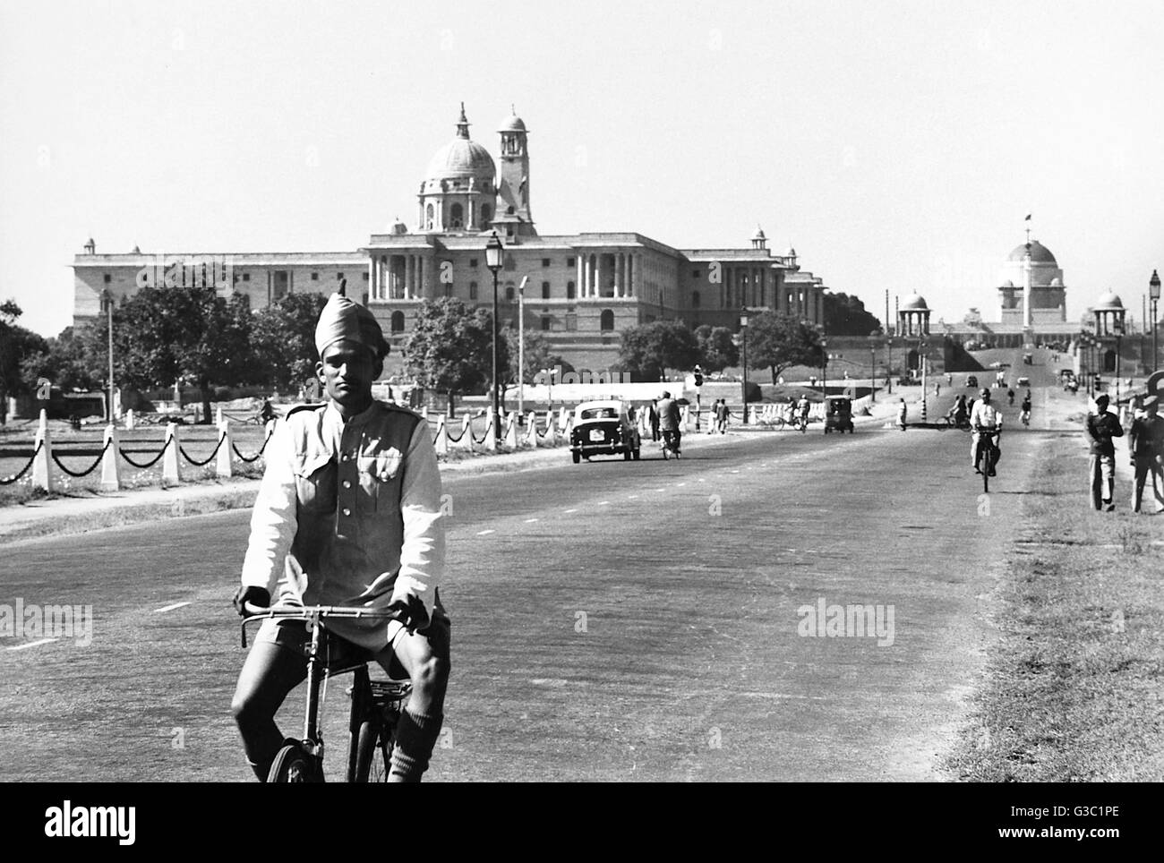 Turbanned ciclista in New Delhi, India, con edifici governativi in background. Data: 1961 Foto Stock