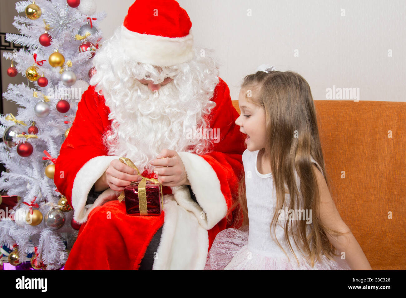 La ragazza con interesse assomiglia a Babbo Natale aiuta ad aprire il suo regalo Foto Stock