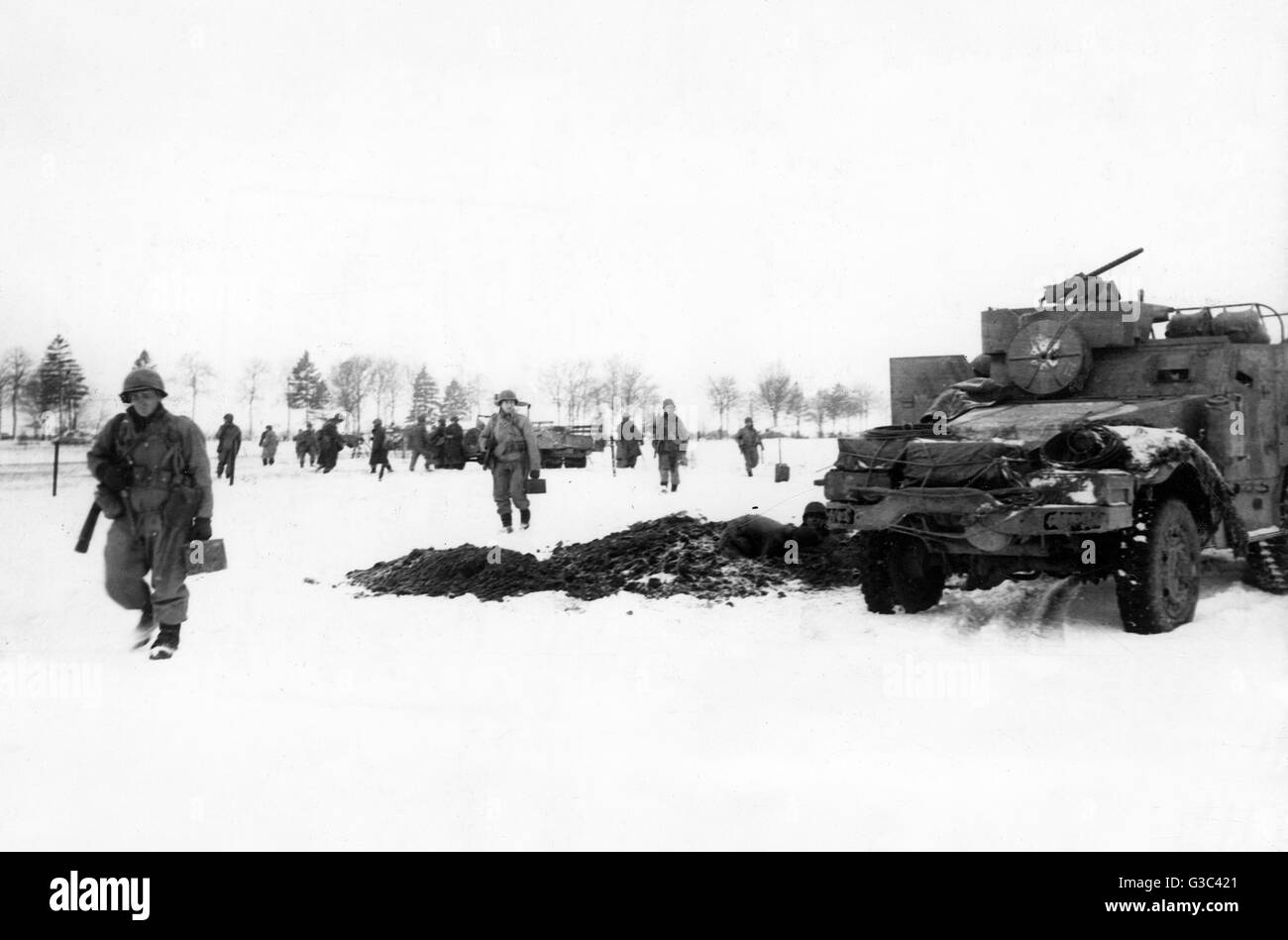 Soldati provenienti da un americano divisione corazzata, supportato da serbatoi, spostare fino ad attaccare un nemico posizione sulla Bastogne fronte durante la Battaglia di Bulge. In primo piano due uomini scavare una foxhole nella coperta di neve terra Data: gennaio 1945 Foto Stock