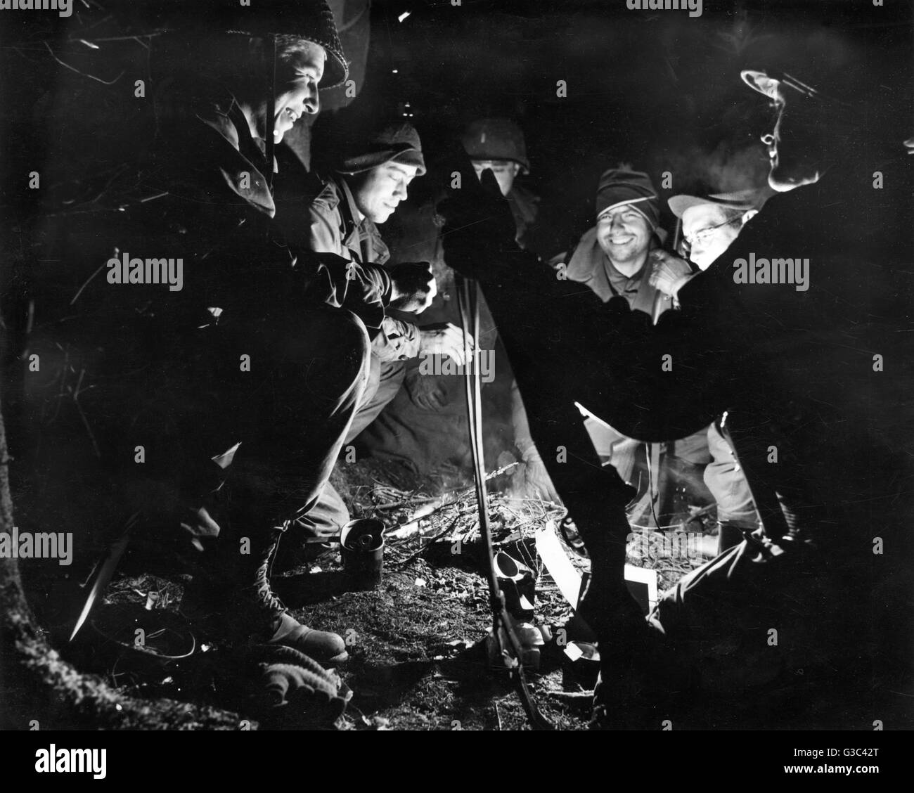 Gli uomini della ottantaduesima U.S. Airborne Division raccogliere tutto il calore e la luce di un fuoco di notte in pesante foresta delle Ardenne, Belgio. Essi erano stati parte di 116 uomini che hanno tenuto un incrocio a ovest di Regne per 76 ore durante la battaglia della Bulg Foto Stock
