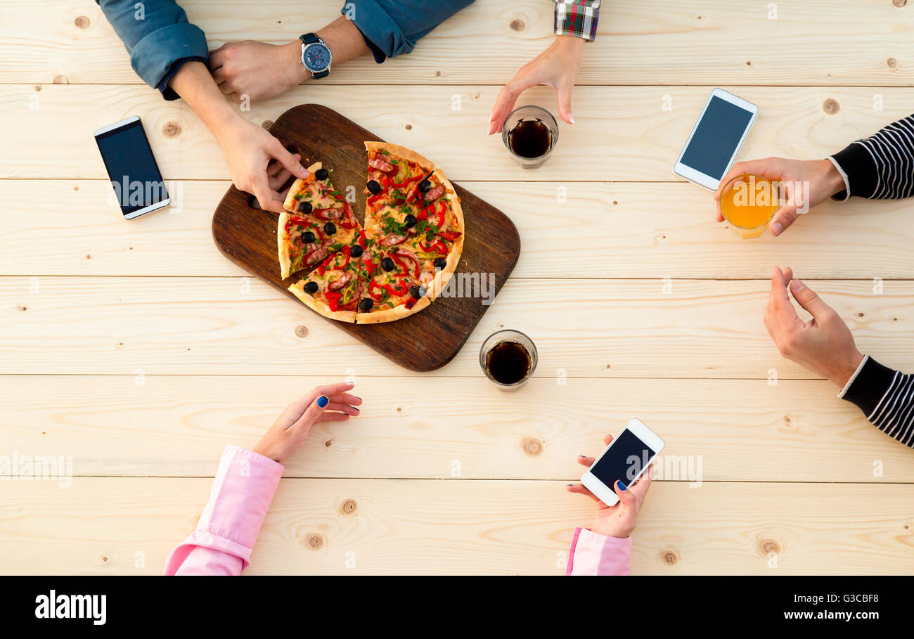 Le mani di persone in legno Cafe tavolo pizza con bevande alimentari e gadget elettronici Foto Stock