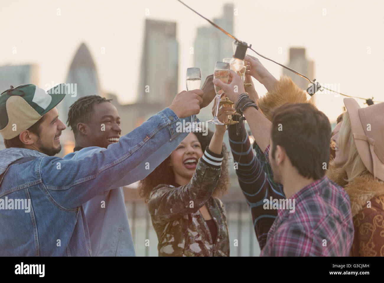 Giovani amici adulti tostatura bicchieri di champagne al partito sul tetto Foto Stock
