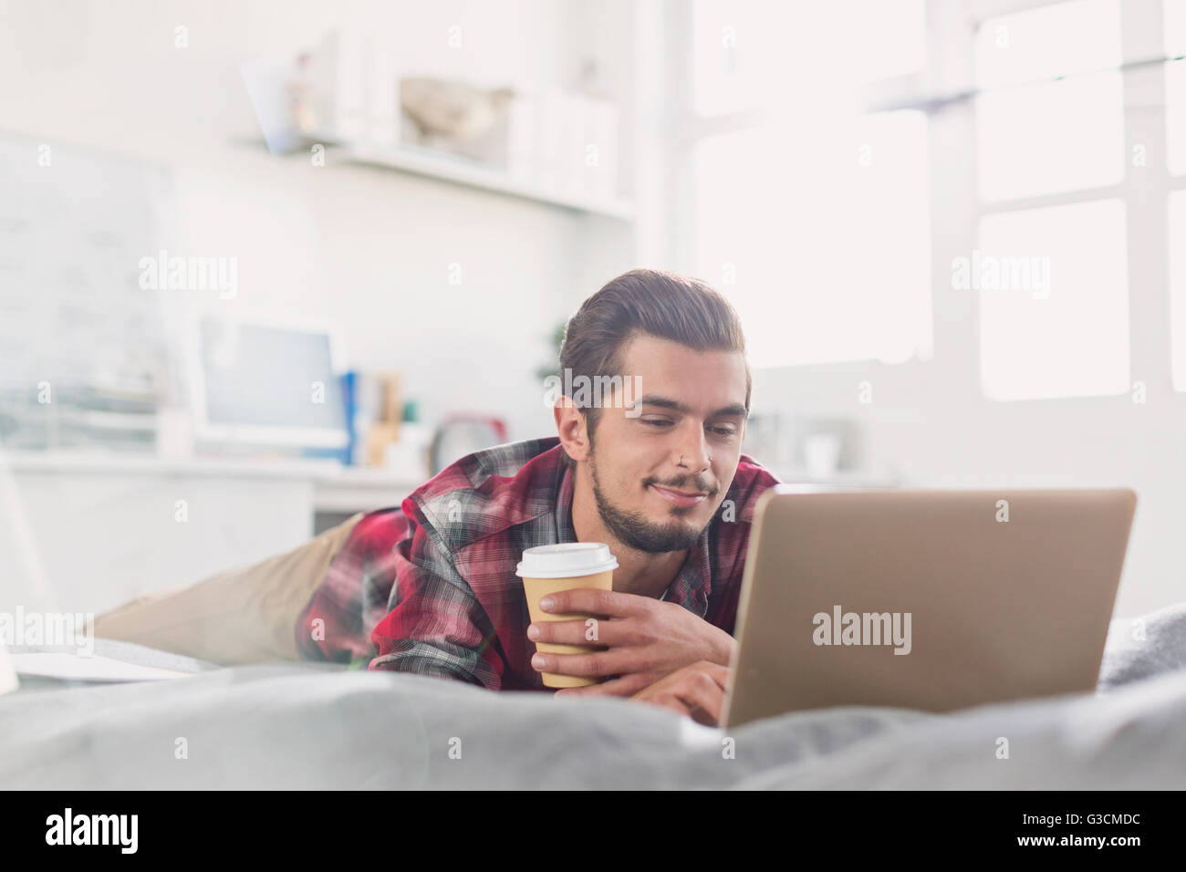 Giovane uomo di bere il caffè al computer portatile sul letto Foto Stock